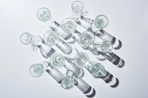 top view of glasses with clear water and shadows on white surface