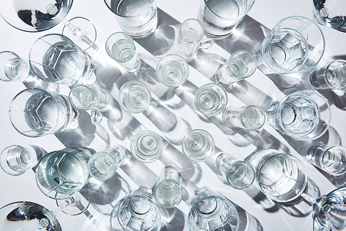 top view of glasses with pure water and shadows on white surface