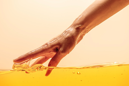 partial view of hand touching yellow bright liquid isolated on yellow