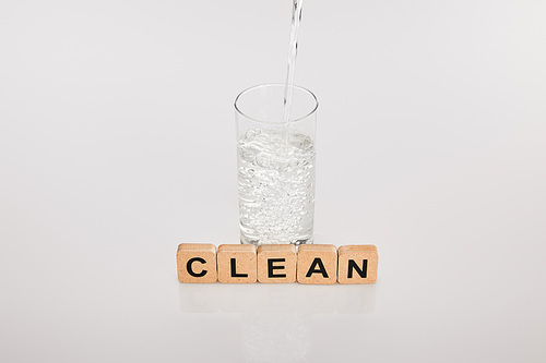 clear fresh water pouring in glass near cubes with clean lettering on grey background