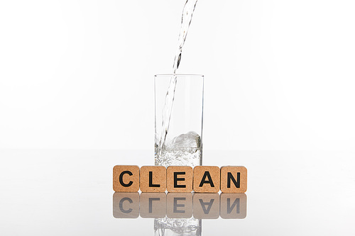 clear fresh water pouring in glass near cubes with clean lettering isolated on white