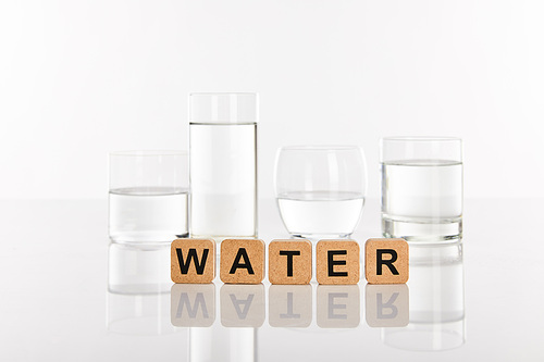 clear fresh water in glasses near cubes with water lettering isolated on white