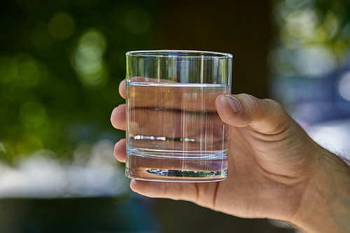 partial view of man holding glass with clear fresh water outdoor