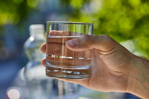 cropped view of man holding glass with clear fresh water outdoor