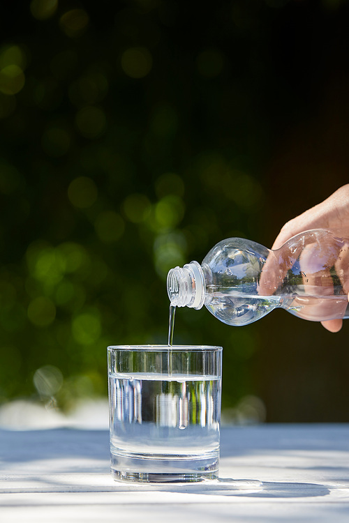 cropped view of man pouring clean water from plastic bottle into glass