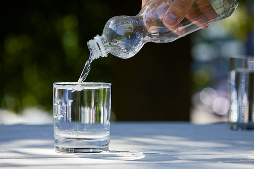 cropped view of man pouring clean water from plastic bottle into glass