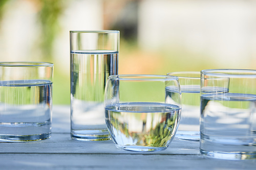 clear fresh water in transparent glasses in sunlight on wooden table