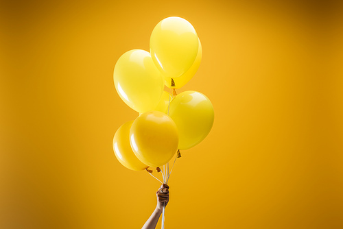 cropped view of woman holding festive bright minimalistic decorative balloons on yellow background