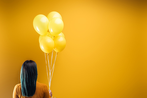 back view of woman holding festive bright balloons on yellow background