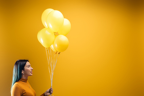 smiling woman holding festive bright decorative balloons on yellow background