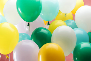close up view of bright green, white, yellow and blue decorative balloons on pink background