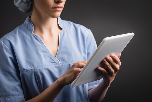 cropped view of nurse in uniform using digital tablet isolated on dark grey