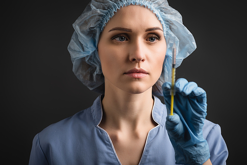 syringe with vaccine in hand of nurse in latex glove on blurred background isolated on dark grey
