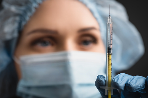 syringe with vaccine near nurse in medical cap on blurred background