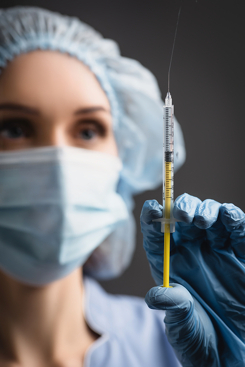 syringe with vaccine splash in hand of nurse in latex glove on blurred background isolated on dark grey