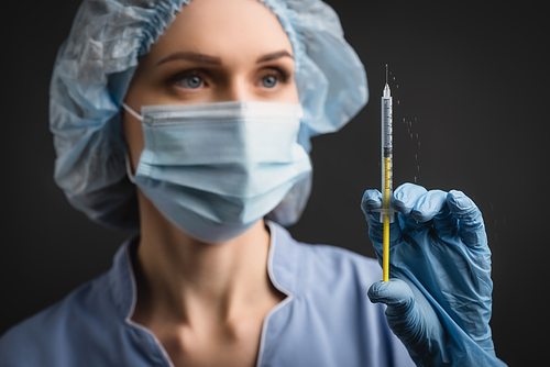 syringe with vaccine splash in hand of nurse in medical mask on blurred background isolated on dark grey