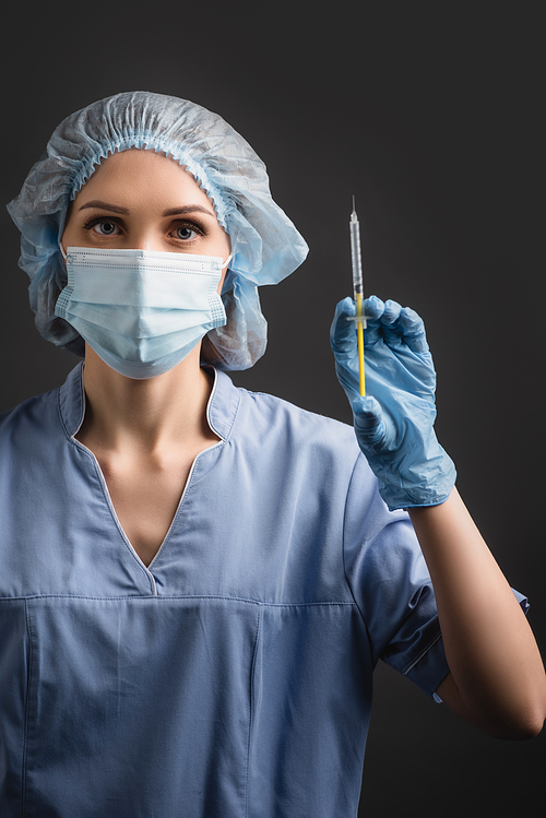 nurse in medical mask holding syringe with vaccine isolated on dark grey