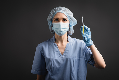 nurse in medical mask and cap holding syringe with vaccine isolated on dark grey