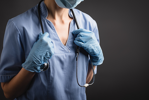 cropped view of nurse in medical mask and latex gloves adjusting stethoscope isolated on dark grey