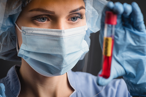 nurse in medical mask holding test tube on blurred foreground isolated on dark grey