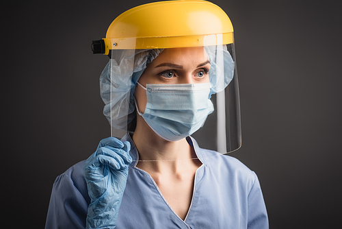 nurse in medical mask, cap and face shield isolated on dark grey