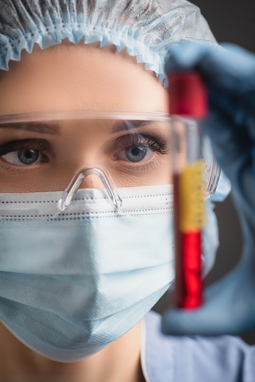 close up of nurse in medical cap, mask and goggles holding test tube on blurred foreground