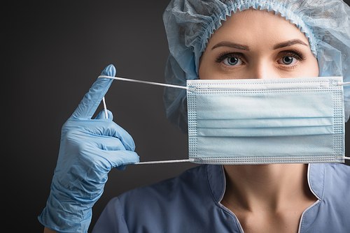 nurse in blue latex gloves wearing medical mask isolated on dark grey