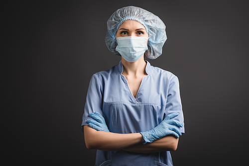 nurse in latex gloves, medical cap and mask standing with crossed arms isolated on dark grey