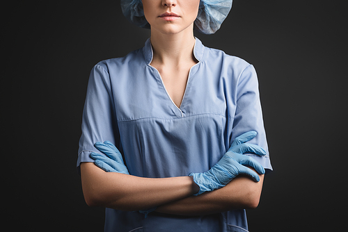 cropped view of nurse in medical cap and latex gloves standing with crossed arms isolated on dark grey