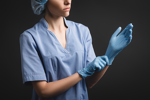 partial view of nurse in medical cap wearing latex gloves isolated on dark grey