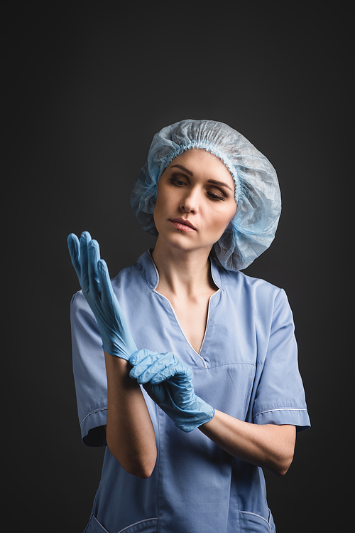 nurse in medical cap wearing latex gloves isolated on dark grey