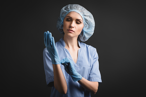 nurse in medical cap wearing blue latex gloves isolated on dark grey
