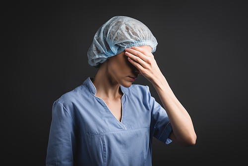 tired nurse in medical cap covering eyes isolated on dark grey