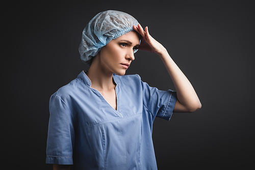 tired nurse in medical cap looking away isolated on dark grey