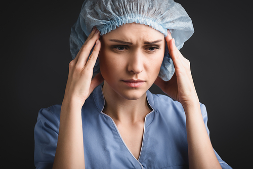 tired nurse in medical cap suffering from headache isolated on dark grey