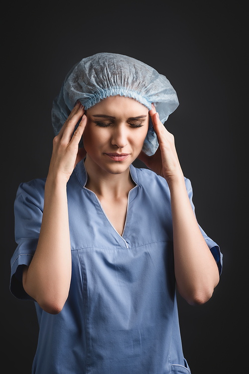 tired nurse with closed eyes suffering from migraine isolated on dark grey