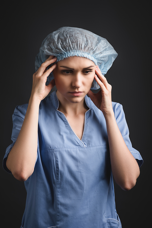 tired nurse in medical cap suffering from migraine isolated on dark grey