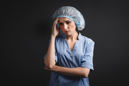 nurse in blue medical cap having headache isolated on dark grey