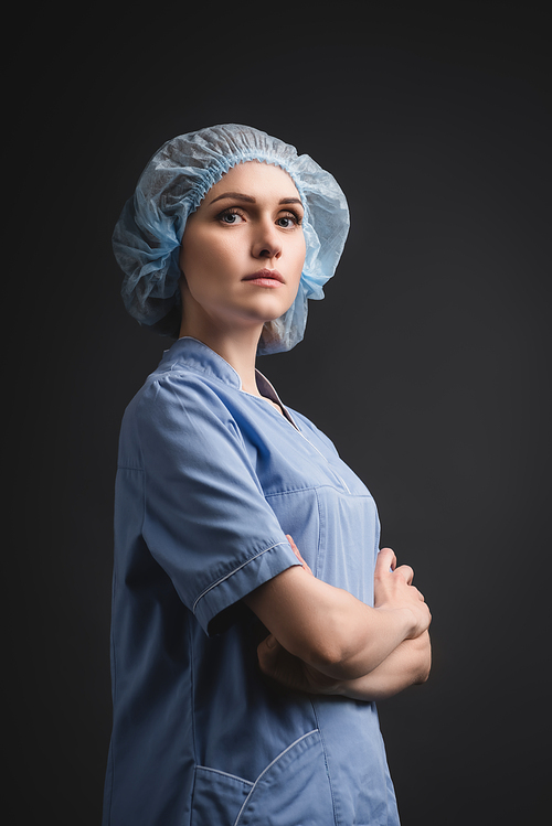 nurse in blue medical cap standing with crossed arms isolated on dark grey