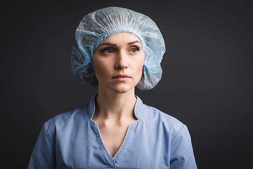 nurse in medical cap looking away isolated on dark grey