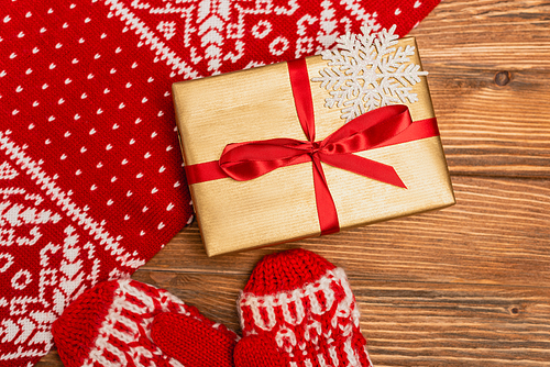 top view of gift box and red knitted scarf and mittens on wooden background