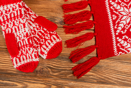 top view of red knitted scarf and mittens on wooden background