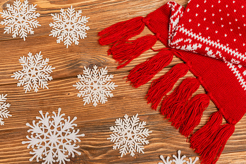 top view of winter snowflakes and red knitted scarf on wooden background