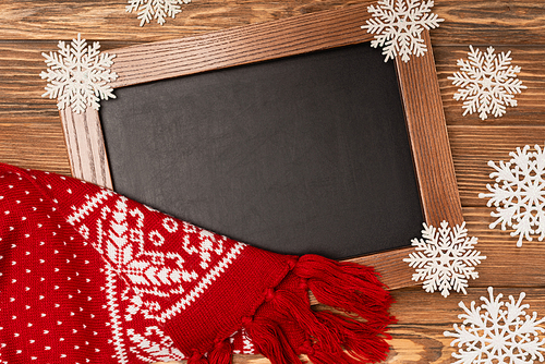 top view of winter snowflakes on chalkboard and knitted scarf on wooden background