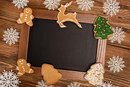 top view of winter snowflakes on chalkboard and Christmas cookies on wooden background
