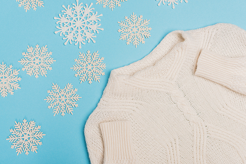 top view of winter white sweater and snowflakes on blue background