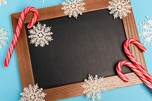 top view of chalkboard, candy canes and snowflakes on blue background
