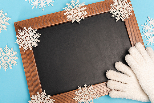 top view of winter white gloves, chalkboard and snowflakes on blue background