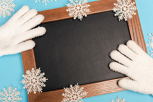 top view of winter white gloves, chalkboard and snowflakes on blue background