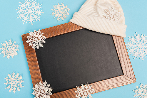 top view of winter white beanie, chalkboard and snowflakes on blue background